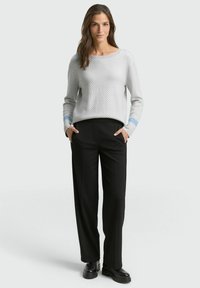 Pull gris clair avec motif texturé et accents bleus, associé à un pantalon large noir et des chaussures noires épaisses.