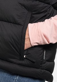 Czarna kamizelka puchowa o teksturowanym wykończeniu, z boczną kieszenią i kontrastującą jasnoróżową koszulą z długim rękawem pod spodem.