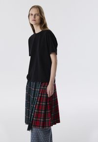 Zwart T-shirt met korte mouwen, gecombineerd met een meerpatronen geplooide rok in groen, rood en marineblauw ruit, met een denim basis en witte stippen.