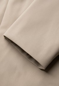 Tessuto beige con una finitura liscia e testurizzata, caratterizzato da bordi piegati. Il materiale appare leggero e morbido. Si notano delle sottili righe.