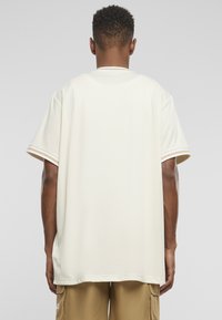 Kortærmet t-shirt i lys beige med en afslappet pasform. Har hvid syning ved kraven og ærmerne. Glat stoftekstur.