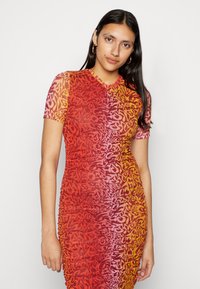 Vestido justo com mangas curtas em degradê de vermelho e amarelo, apresentando um padrão texturizado e um design drapeado nas laterais.