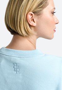 Polo azzurro chiaro con colletto a costine, caratterizzato da un logo ricamato in un colore a contrasto sul retro. Materiale in cotone morbido, vestibilità casual.