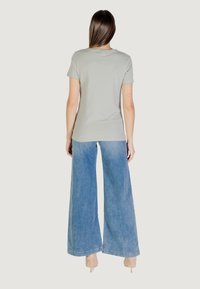 T-shirt grigio chiaro a maniche corte abbinato a jeans in denim blu chiaro a gamba larga. Il tessuto sembra morbido, con una vestibilità casual e senza motivi visibili.