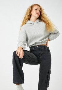 Sudadera recortada gris claro con puños elásticos, combinada con pantalones cargo negros de talle alto que presentan un detalle de bolsillo lateral. Zapatillas blancas.