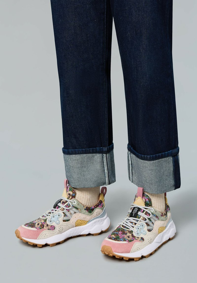 Chaussures de sport colorées avec des motifs floraux ; les matériaux incluent du daim et du mesh dans des nuances de rose, bleu et beige ; design de semelle épaisse.