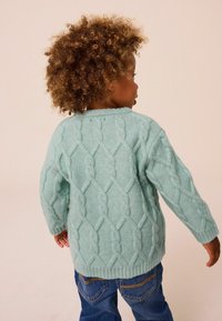 Pull en maille torsadée bleu clair avec un motif texturé, doté de manches longues et d'un col rond, porté sur un jean bleu.