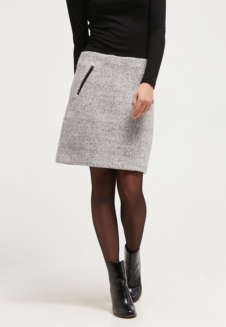 Femme portant une jupe grise en laine longueur genou avec une poche zippée noire, associée à des collants noirs transparents et des bottines noires.