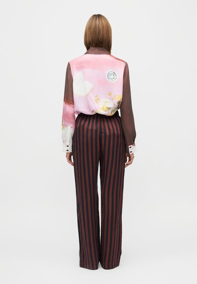 Dlhá ružová priesvitná blúzka s kvetinovými motívmi, v páre s vysokými širokými nohavicami s vertikálnymi červenými a čiernymi pruhmi.