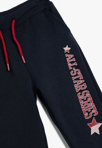 Marineblaue Sweatpants mit roten Kordeln und "ALL-STAR SERIES" vertikal in weißen und roten Buchstaben aufgedruckt, mit einem roten Sternakzent.