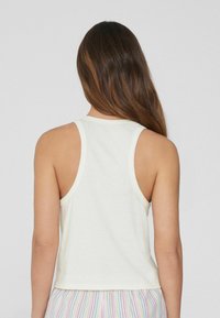 Top sin mangas de algodón blanco con diseño de espalda nadadora. El dobladillo cae a la altura de la cintura, presenta una textura sutil y se combina con pantalones de pijama a rayas.