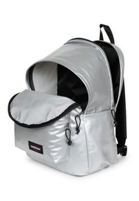 Srebrny plecak z błyszczącego, odbijającego materiału, z czarnym wykończeniem, przednią klapą i regulowanymi szelkami. Otwarty dla łatwego dostępu do wnętrza.
