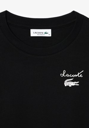 Mustast puuvillane T-särk, ümmarguste kaelustega. Eest leidub valge "Lacoste" logo ja krokodilli graafika. Mugav lõige, suurus 36.