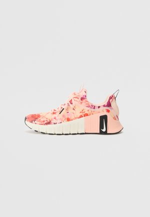 Zapatilla Nike con estampado floral en tonos rosa y melocotón, suela blanca y logo negro en el talón, mostrada de perfil sobre un fondo liso.