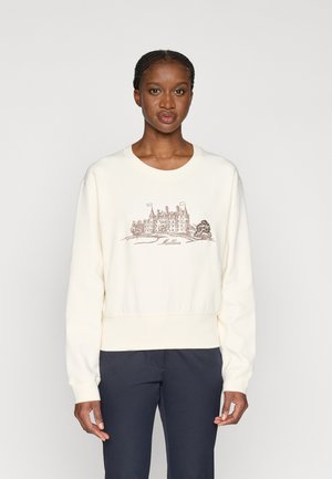 Lichtcrème sweatshirt met een ribbelzoom en manchetten, met een bruine afbeelding van een gebouw met bomen, gecentreerd op de voorkant.