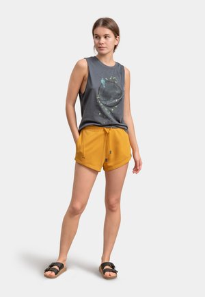 Grijze mouwloze shirt met vogelafbeelding; gele stringschoenen; zwarte sandalen; licht materiaal, relaxed fit, minimalistisch design.