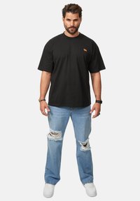 Black cotton t-shirt with a round neckline, worn with light blue distressed jeans featuring large rips at the knees, and white sneakers.