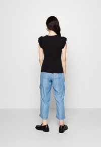 Top nero con maniche corte a volant, abbinato a pantaloni cargo azzurri chiari e scarpe nere. Tessuto morbido con una silhouette aderente.