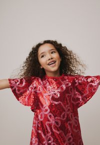 Abito rosso di paillettes con maniche a svolazzo e un motivo giocoso di anelli rosa, che riflette la luce con una texture lucida.