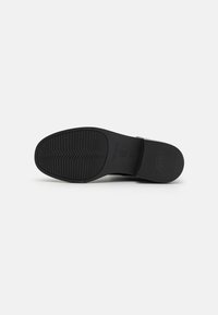 Black shoe sole with a textured tread pattern. Features a flat design and a smooth finish. Marked with sizing and brand information.