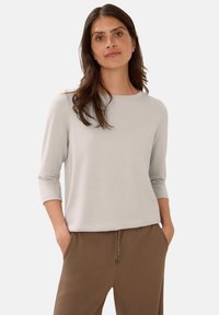 Light gray, three-quarter sleeve top with a round neckline, soft texture, paired with brown pants featuring an elastic waistband and drawstring.