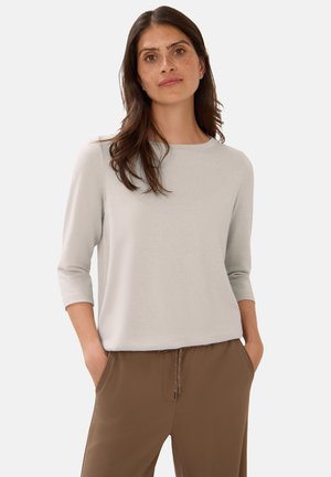 Haut gris clair à manches trois-quarts avec un col rond, texture douce, associé à un pantalon marron avec une taille élastique et un cordon de serrage.