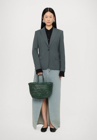 Blazer gris ajusté sur une chemise noire, associé à une jupe maxi en denim avec une fente à l'avant. Sac en osier vert et chaussures noires.