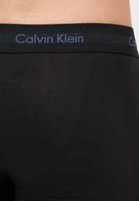 Μαύρο βαμβακερό μποξεράκι με φαρδύ ελαστικό κορδόνι και λογότυπο 'Calvin Klein' σε σκούρο μπλε. Απαλή υφή, εφαρμοστό σχέδιο.