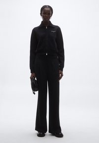 Fekete cipzáras pulóver két első zsebbel és "tommy" logóval, magas derekú fekete bő szárú nadrággal és egy kis fekete táskával párosítva.