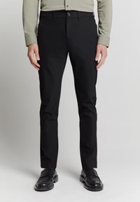 Zwarte broeken met een rechte pasvorm, gemaakt van gladde stof, met een knoopsluiting en zijzakken, gecombineerd met zwarte leren schoenen.