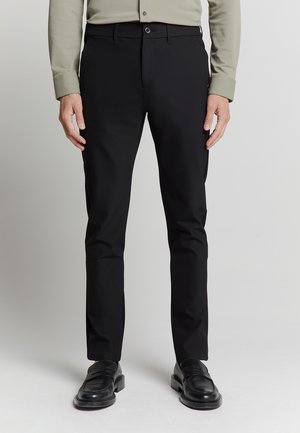 Zwarte broeken met een rechte pasvorm, gemaakt van gladde stof, met een knoopsluiting en zijzakken, gecombineerd met zwarte leren schoenen.