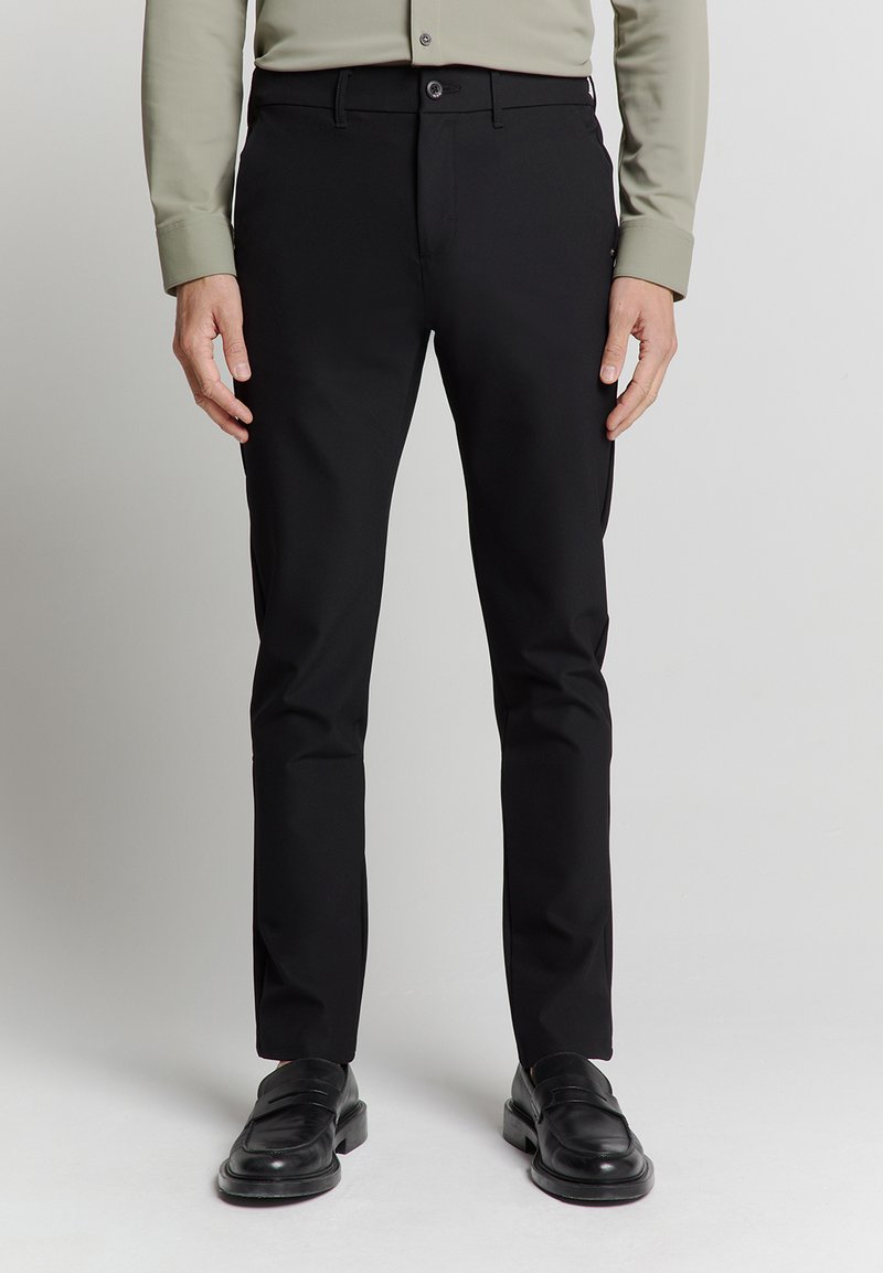 Zwarte broeken met een rechte pasvorm, gemaakt van gladde stof, met een knoopsluiting en zijzakken, gecombineerd met zwarte leren schoenen.