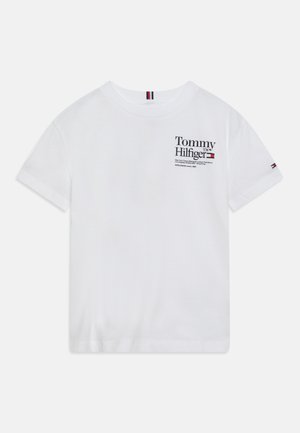 Biała koszulka z krótkim rękawem z logo "Tommy Hilfiger" i listą miast nadrukowaną na czarno na górnej lewej części klatki piersiowej, mała flaga na lewym rękawie.