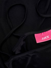 Fekete szövet felső vékony pántokkal, pink címkével, amelyen az "JJXX" felirat található. Az anyag sima, a varratok láthatóak.