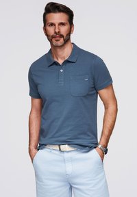 Ljusblå pikétröja med texturerad yta, med krage, en bröstficka och knappslå. Kompletteras av ljusa shorts.