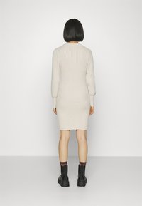 Sukienka dzianinowa w jasnym beżu, o prążkowanej strukturze, dopasowanym kroju, z długimi rękawami i okrągłym dekoltem, zestawiona z czarnymi, masywnymi botkami i wzorzystymi skarpetkami.