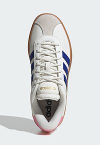 Biały but sportowy z niebieskimi paskami, zamszowym noskiem i gumową podeszwą w kolorze brązowym. Posiada sznurowadła oraz złote logo "adidas". Miękka, teksturowana podszewka wewnętrzna.