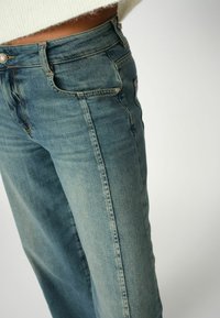Brede pijpen jeans in lichtblauwe denim, met een hoge taille, vijf zakken en zichtbare stikseldetails. Zachte textuur met een vervaagde afwerking.