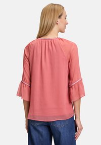 Blusa color pesca con maniche trasparenti a tre quarti, polsini arricciati e texture sottile. Presenta un collo arricciato e un fit morbido.