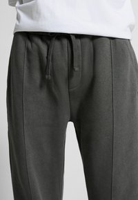 Donkergrijze joggingsbroek met een trekkoord in de taille, gedragen met een wit T-shirt, met zichtbare naden en textuur van de stof.