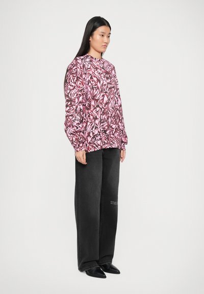 Top largo de manga larga con estampado floral en rosa y mangas globo, combinado con vaqueros oscuros de pierna ancha que presentan texto bordado en la pierna izquierda.