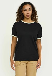 T-shirt en coton noir avec un col en côtes beige clair et des poignets. Manches courtes, coupe décontractée et texture lisse. Simplicité notable dans le design.