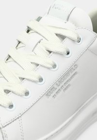 Białe skórzane sneakersy z białymi sznurówkami, niebieskimi oczkami i debiutującym napisem "KARL LAGERFELD 21 RUE ST-GUILLAUME PARIS" na boku.