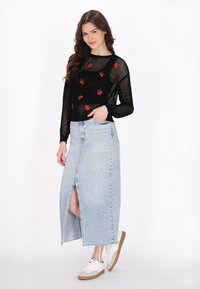 Schwarzer Mesh-Pullover mit roter floraler Stickerei, kombiniert mit einem hellblauen Jeansrock mit Schlitz vorne und fransigem Saum, getragen mit weißen Sneakers.