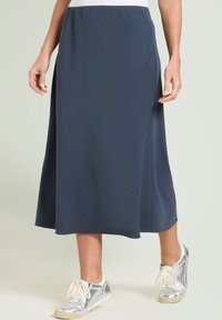 Granatowa spódnica midi z miękkiego materiału, z elastycznym paskiem w talii i zwiewnym krojem. Skomponowana ze srebrnymi trampkami dla casualowego wyglądu.