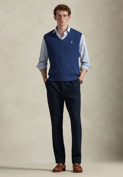 Σκούφο με πλεκτό μοτίβο σε ναυτικό μπλε χρώμα πάνω από ένα ανοιχτό μπλε πουκάμισο με καρό, συνδυασμένο με σκούρο παντελόνι και καφέ δερμάτινα παπούτσια. Ασημένιο ρολόι στον καρπό.