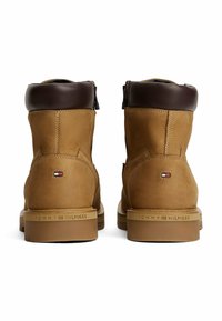 Par de botas de tobillo de cuero marrón claro con cuellos acolchados en marrón oscuro, suelas de marca y pequeñas banderas de Tommy Hilfiger en la parte trasera.