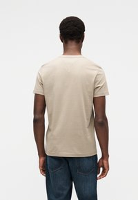 Μπεζ βα μβακερό t-shirt με κοντά μανίκια, κανονικό στρογγυλό λαιμό και μίνιμαλ σχεδιασμό. Φοριέται με σκουρόχρωμο τζιν.