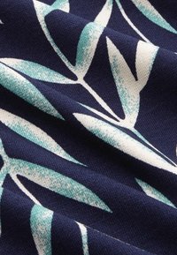 Tummansininen kangas, jossa on vaalean teal- ja kermanväristen lehtien kuviot, joka on pehmeästi teksturoitu ja jossa on näkyviä ompelutietoja.