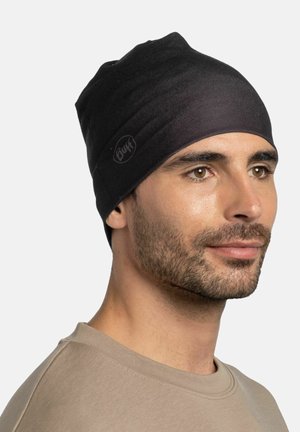 Un gorro de punto negro con una textura suave, que presenta una sutil etiqueta de logo. El sombrero se ajusta cómodamente en la cabeza, cubriendo las orejas.